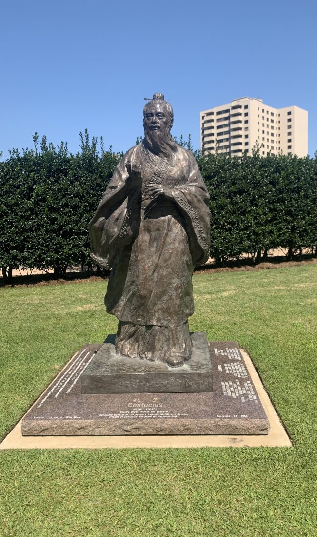 Bronze statue of Confucius standing on a stone plinth in a park